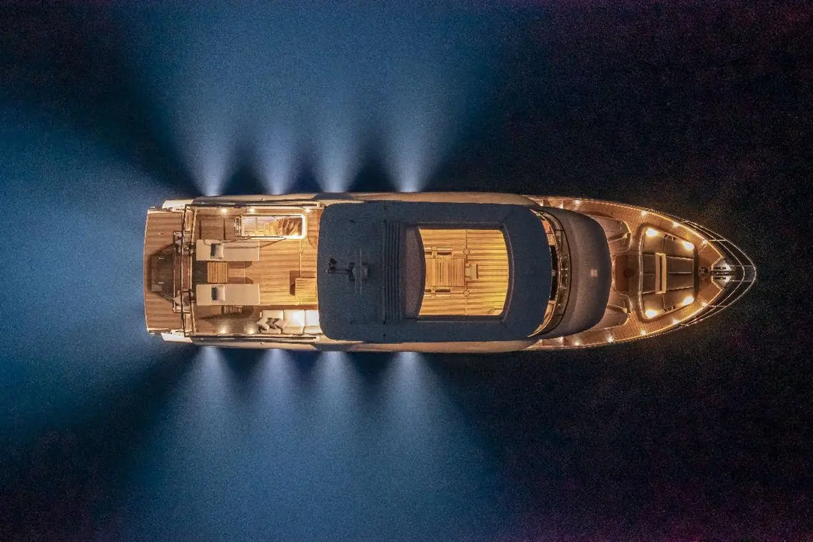 Luxury yacht illuminated at night, showcasing wooden deck and modern seating, surrounded by dark blue water.